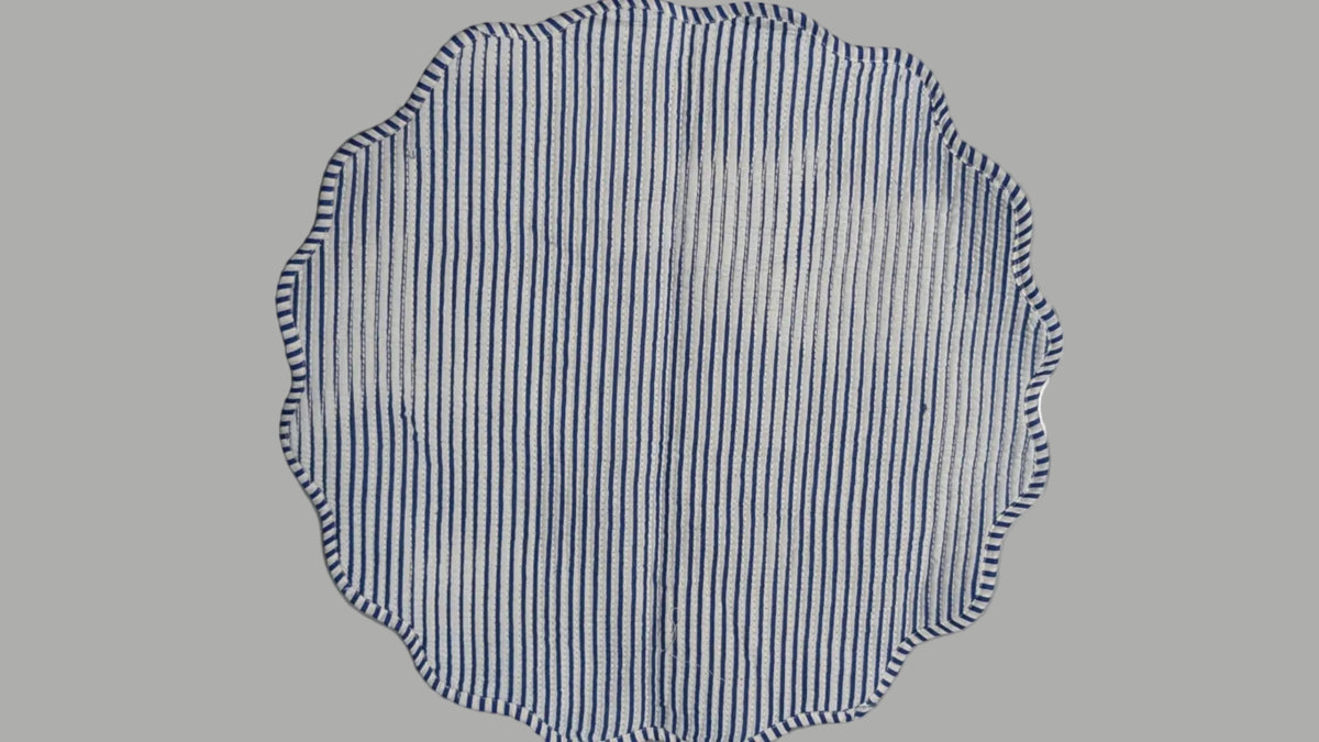 A round, scalloped-edge dishcloth with blue and white horizontal stripes, laid flat on a light gray appliance surface.
