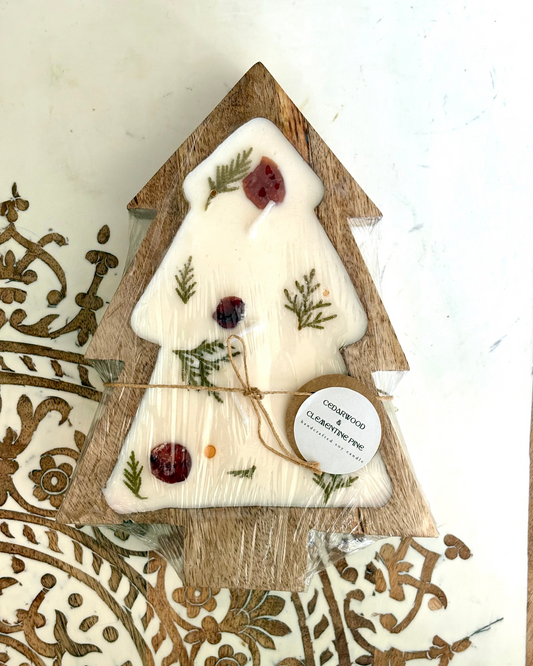 Decorative candle shaped like a Christmas tree with natural elements in a wooden holder.
