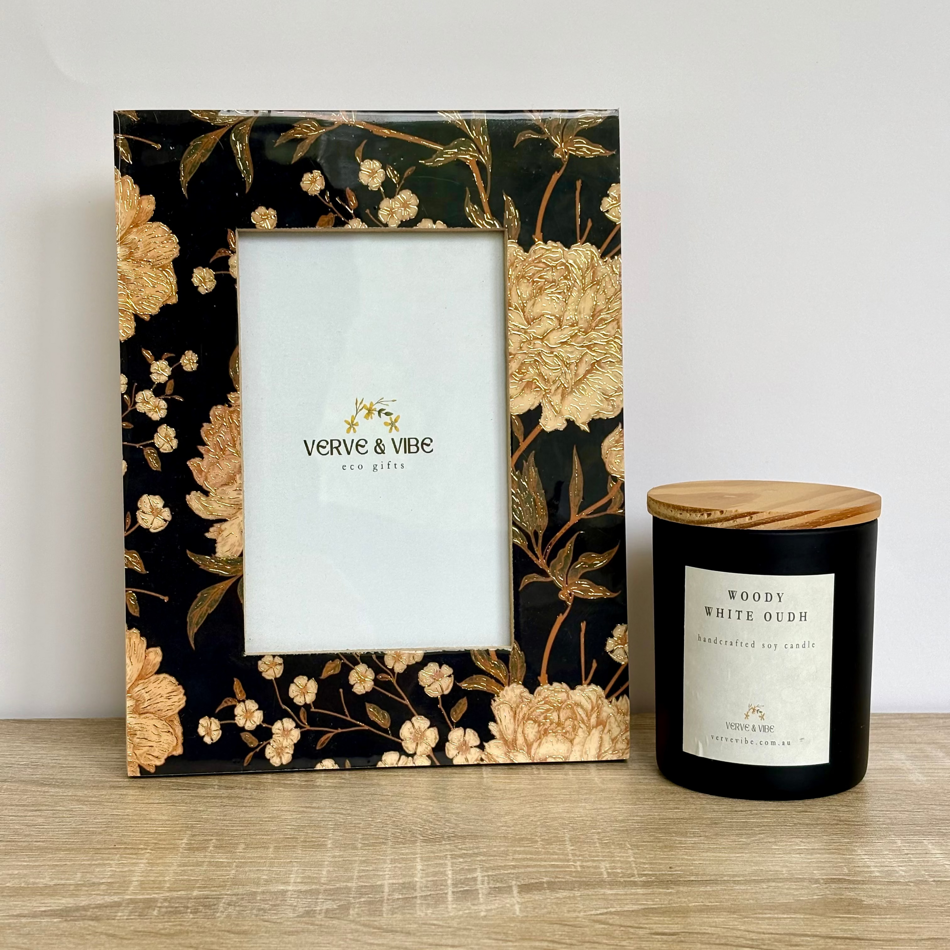 Decorative photo frame with floral design and a candle on a wooden surface.