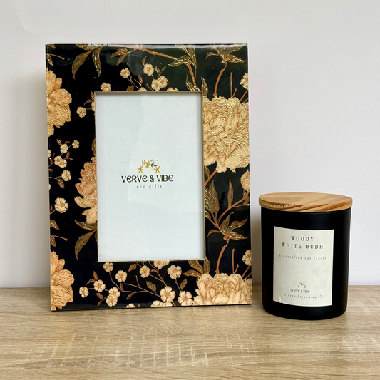 Decorative photo frame with floral design and a candle on a wooden surface.