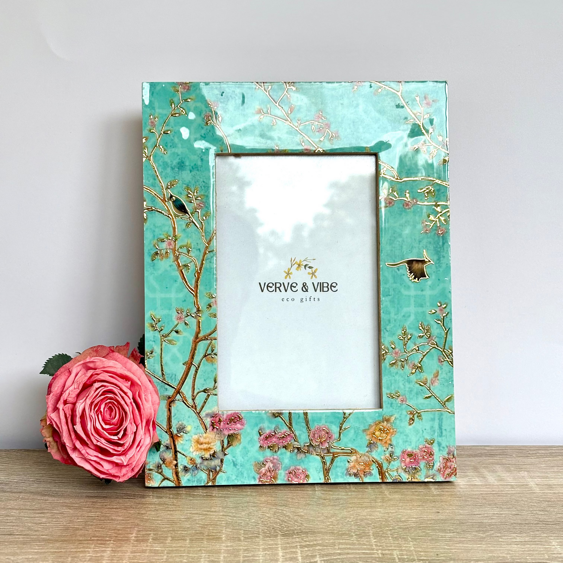 Decorative picture frame with floral design on a wooden surface, featuring the brand 'Verve & Vibe'.