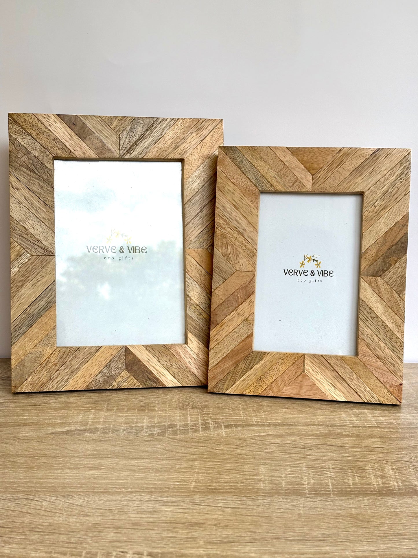 Two wooden picture frames with a herringbone pattern on a wooden surface.