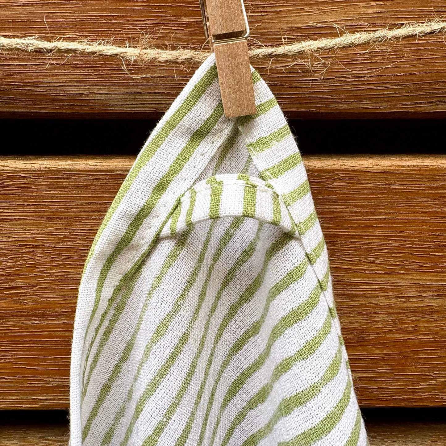 Striped green and white towel hanging on a wooden surface with a wooden clip.