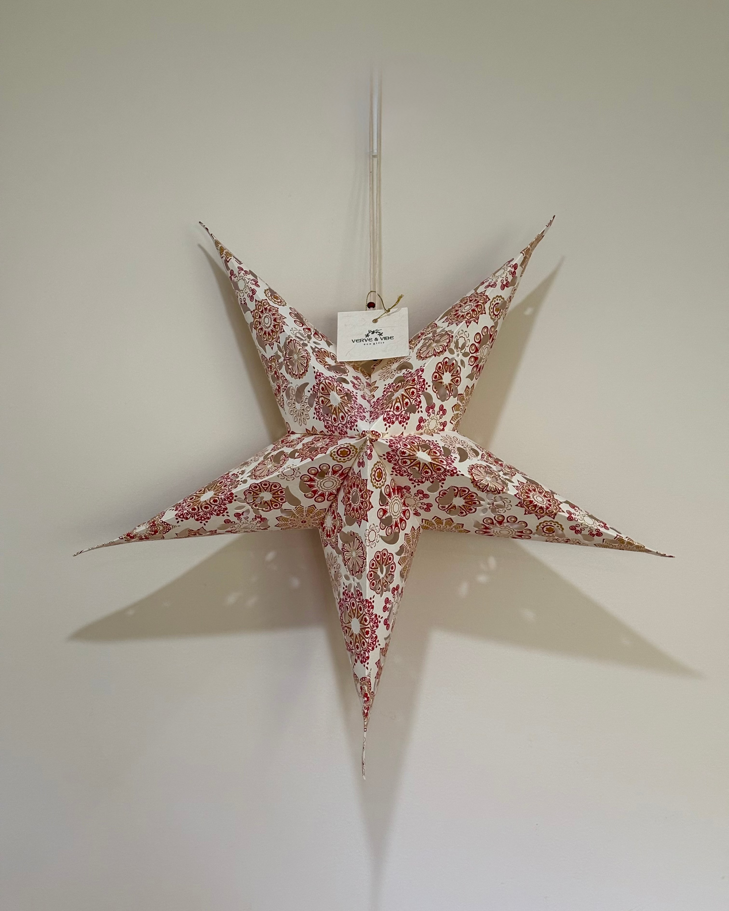 Decorative star hanging on a plain wall with a visible brand tag.