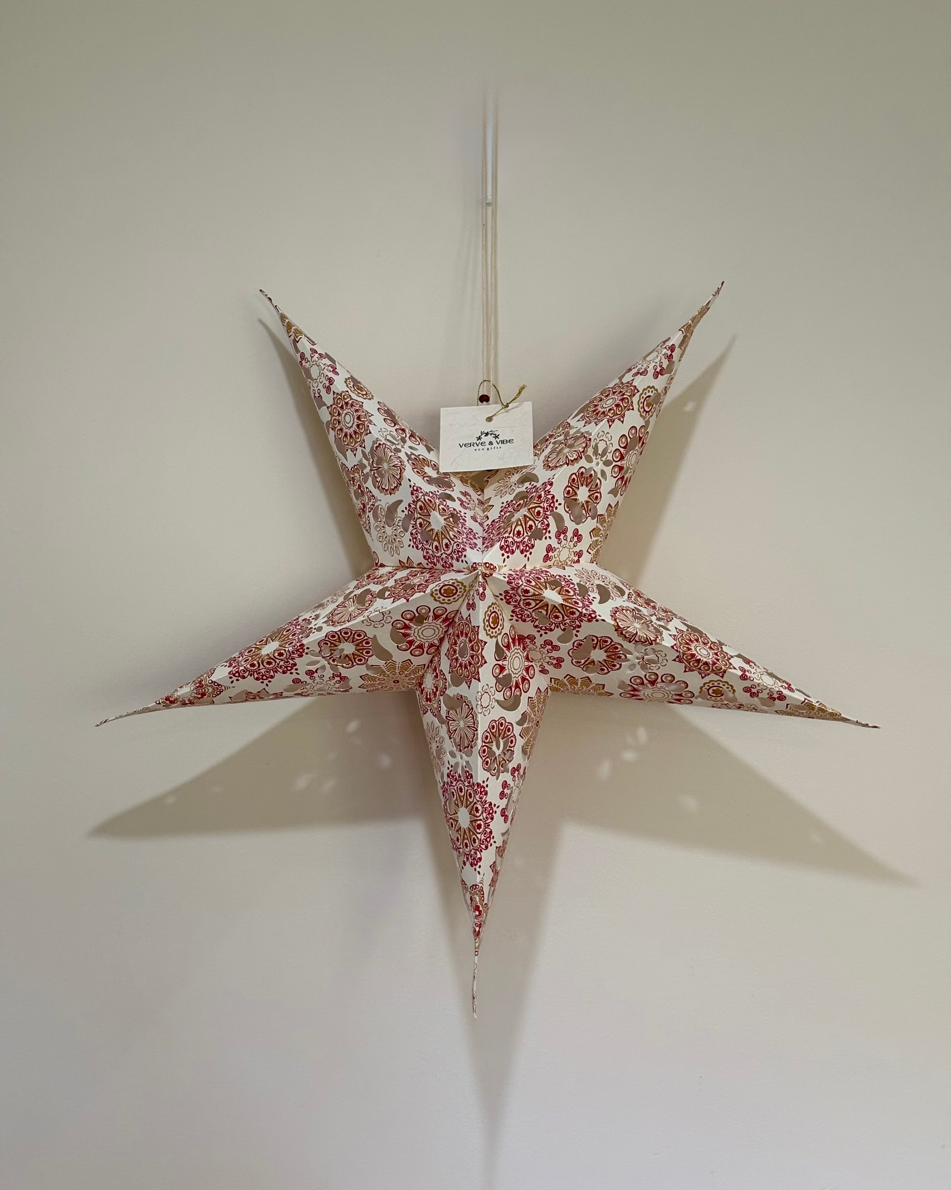 Decorative star hanging on a plain wall with a visible brand tag.