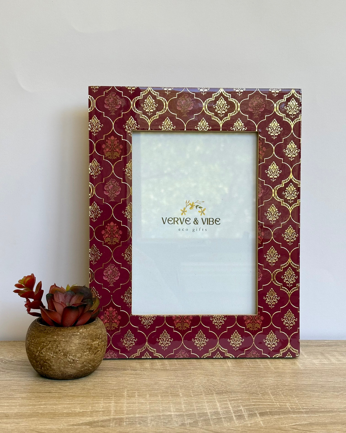 Decorative photo frame with gold patterns on a wooden surface next to a small plant.