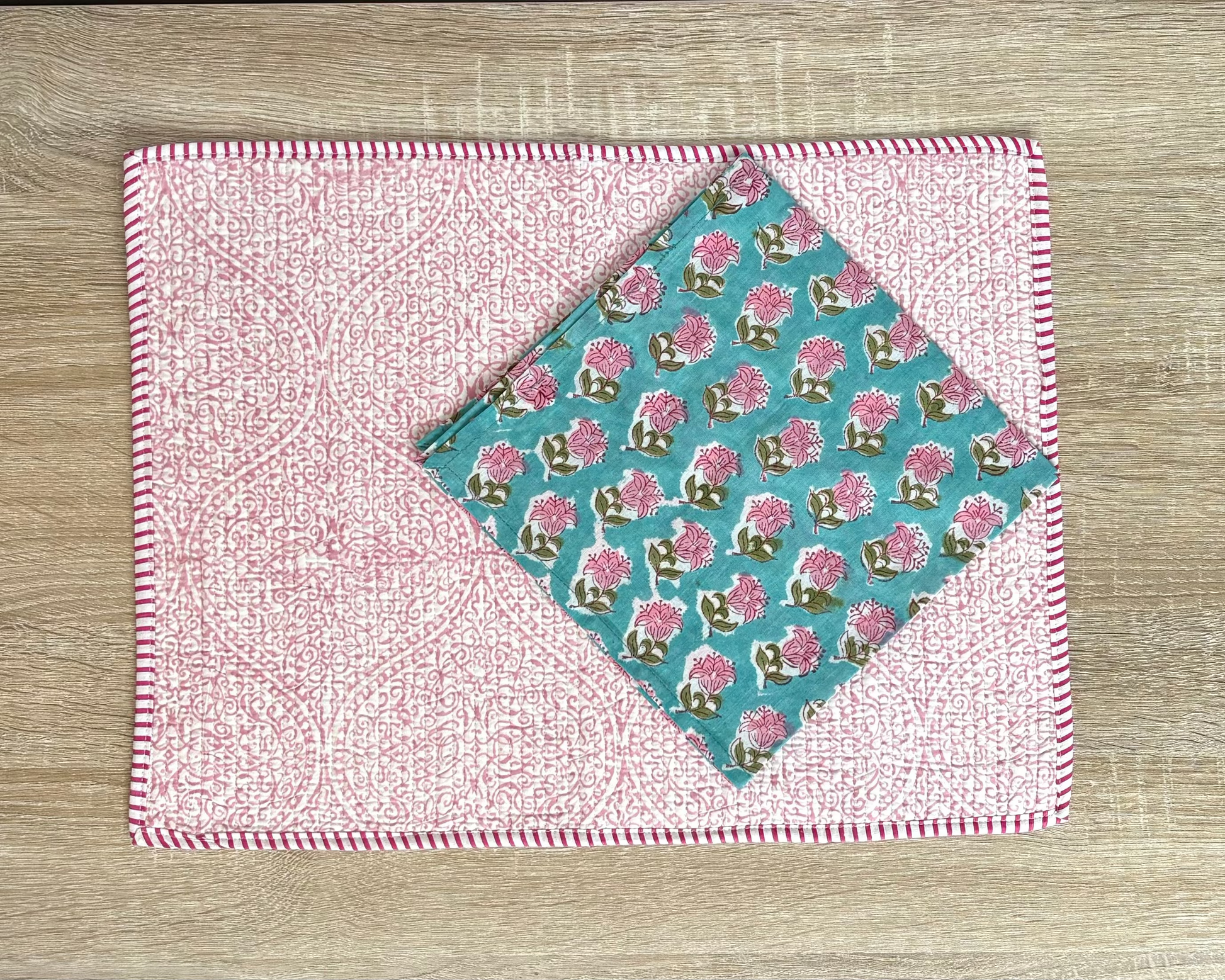 Two fabric samples on a wooden surface, one pink with white pattern and the other teal with floral pattern.