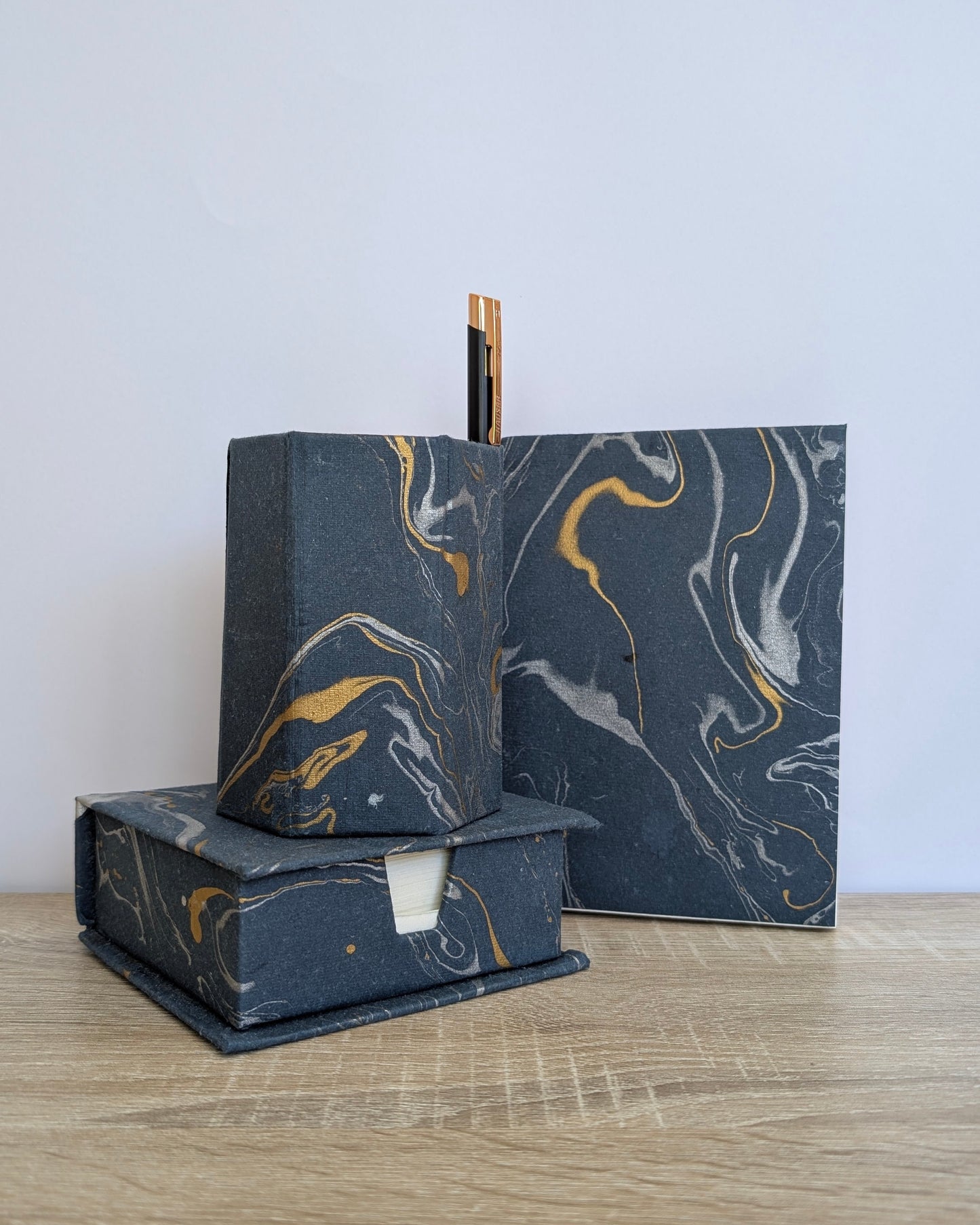Marble-textured black and gold soap bars on a wooden surface with a light gray background