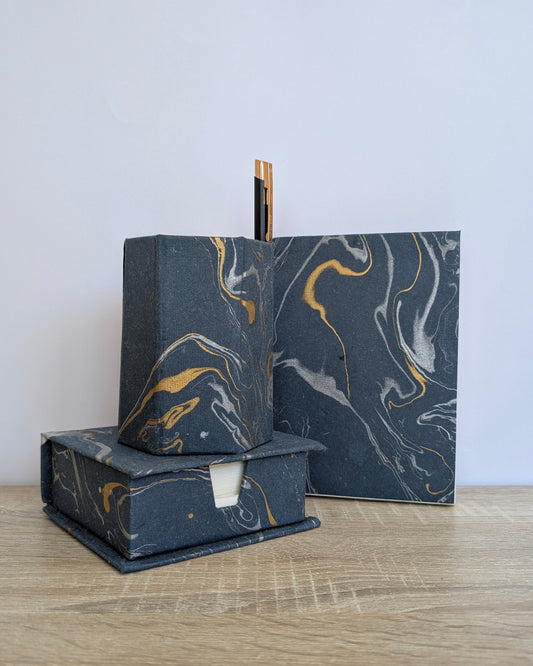 Marble-textured black and gold soap bars on a wooden surface with a light gray background